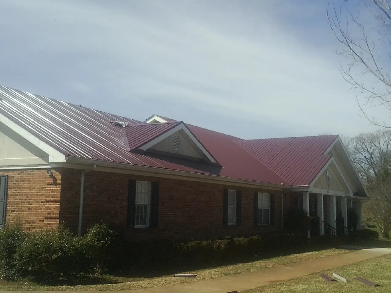 Red metal roof with gabled entries on a long brick building, from a Hail Damage Roof Repair job in Penfield