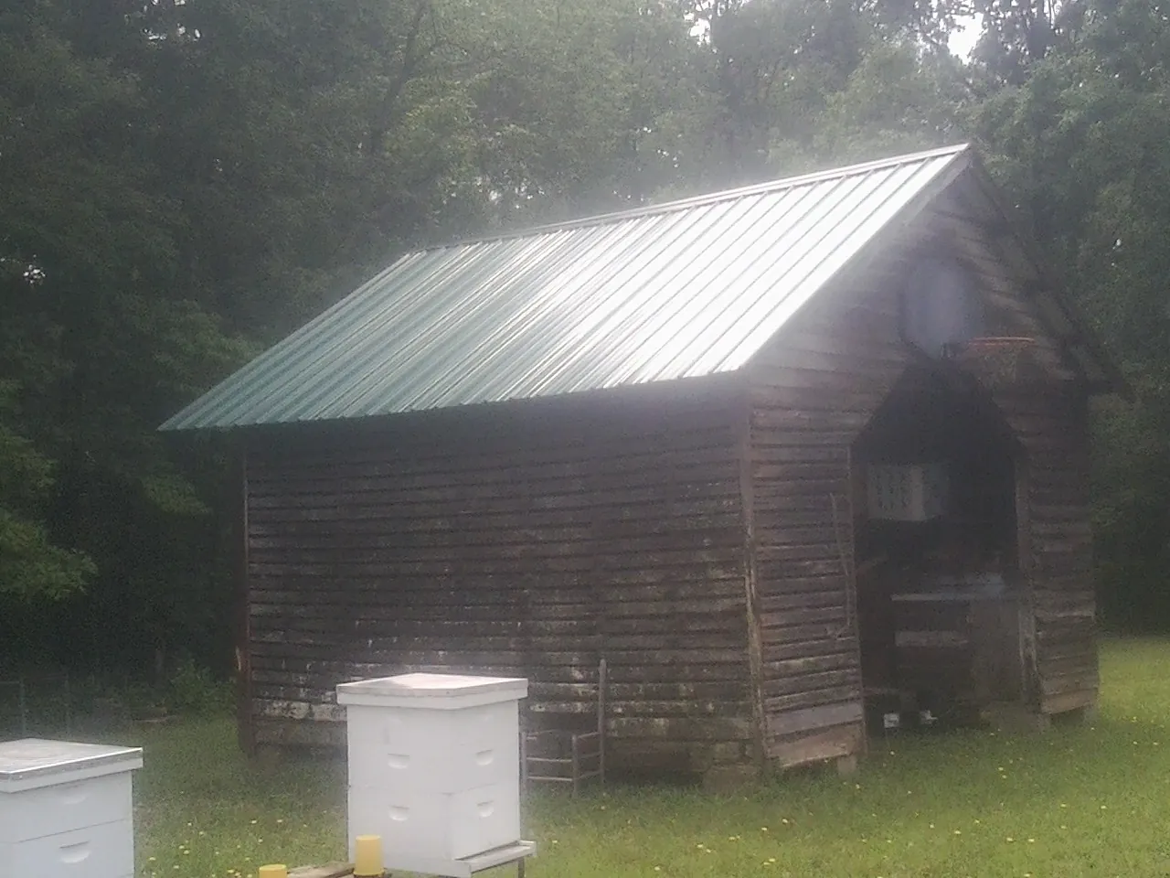Green metal roof on a weathered barn beside stacked beehives in Penfield