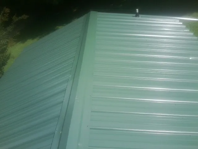 New green metal panels meeting at the ridge of a roof — Flat Roof Repair work by our crew in Penfield