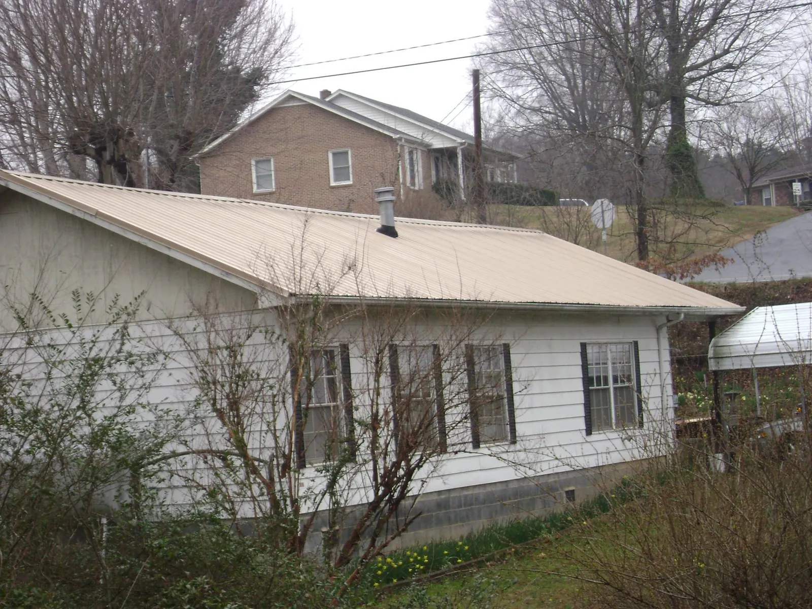 Tan metal roof on a white sided house set into a hillside — Commercial Roofing by Roofing Brothers in Penfield