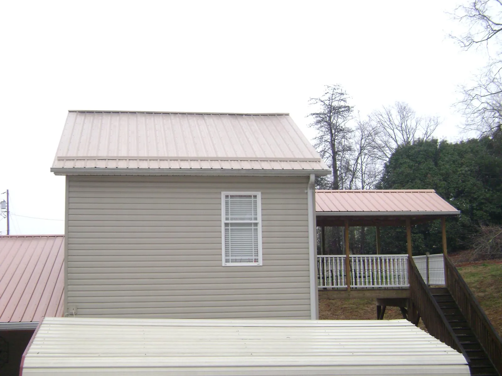 Tan metal roofs on a two story addition and attached porch, from a Roof Replacement job in Penfield